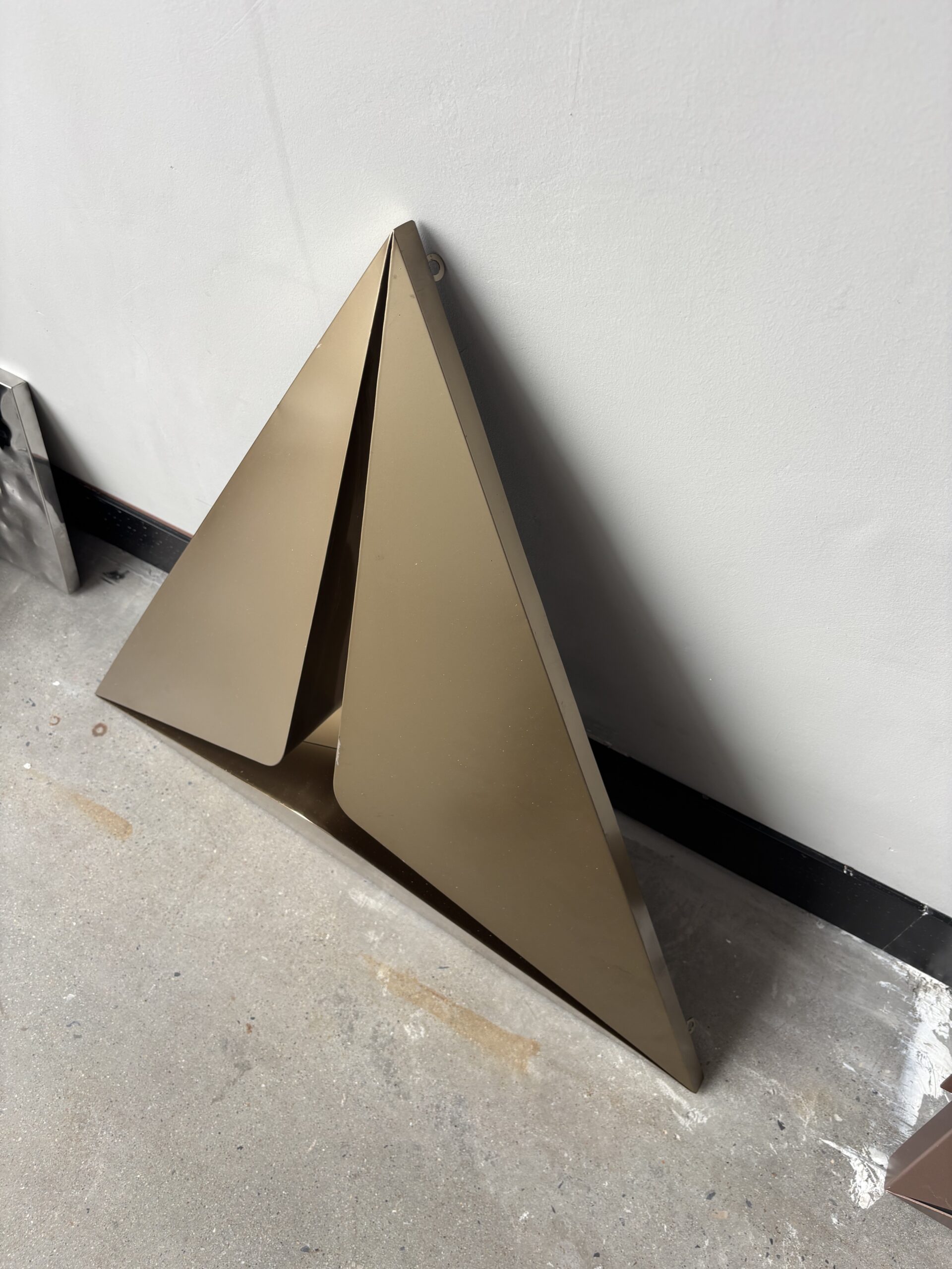 Bronze triangular folded stainless steel honeycomb decorative panel standing against a wall, showing geometric 3D relief.
