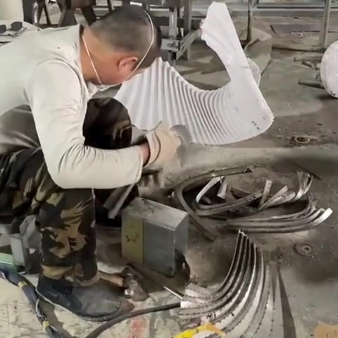 Workshop fabrication of a twisted ribbon sculpture in stainless steel — worker hand-grinding welds