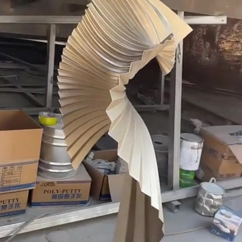 Tall twisted ribbon sculpture in champagne gold stainless steel rising as a loose spiral helix inside a hotel lobby.