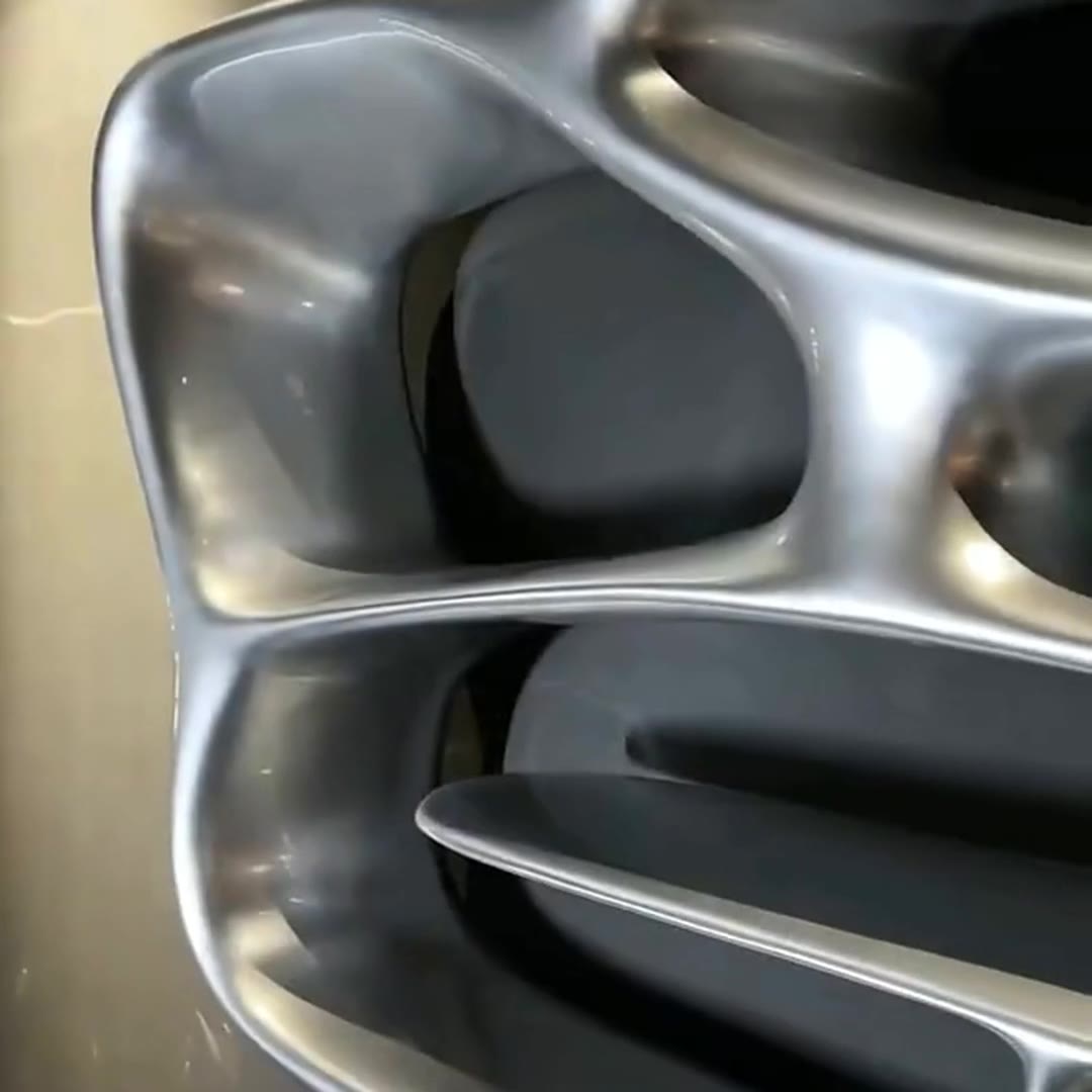 Macro detail of the mirror-polished stainless steel surface, showing flowing organic ridges and an elongated shelf opening under warm light