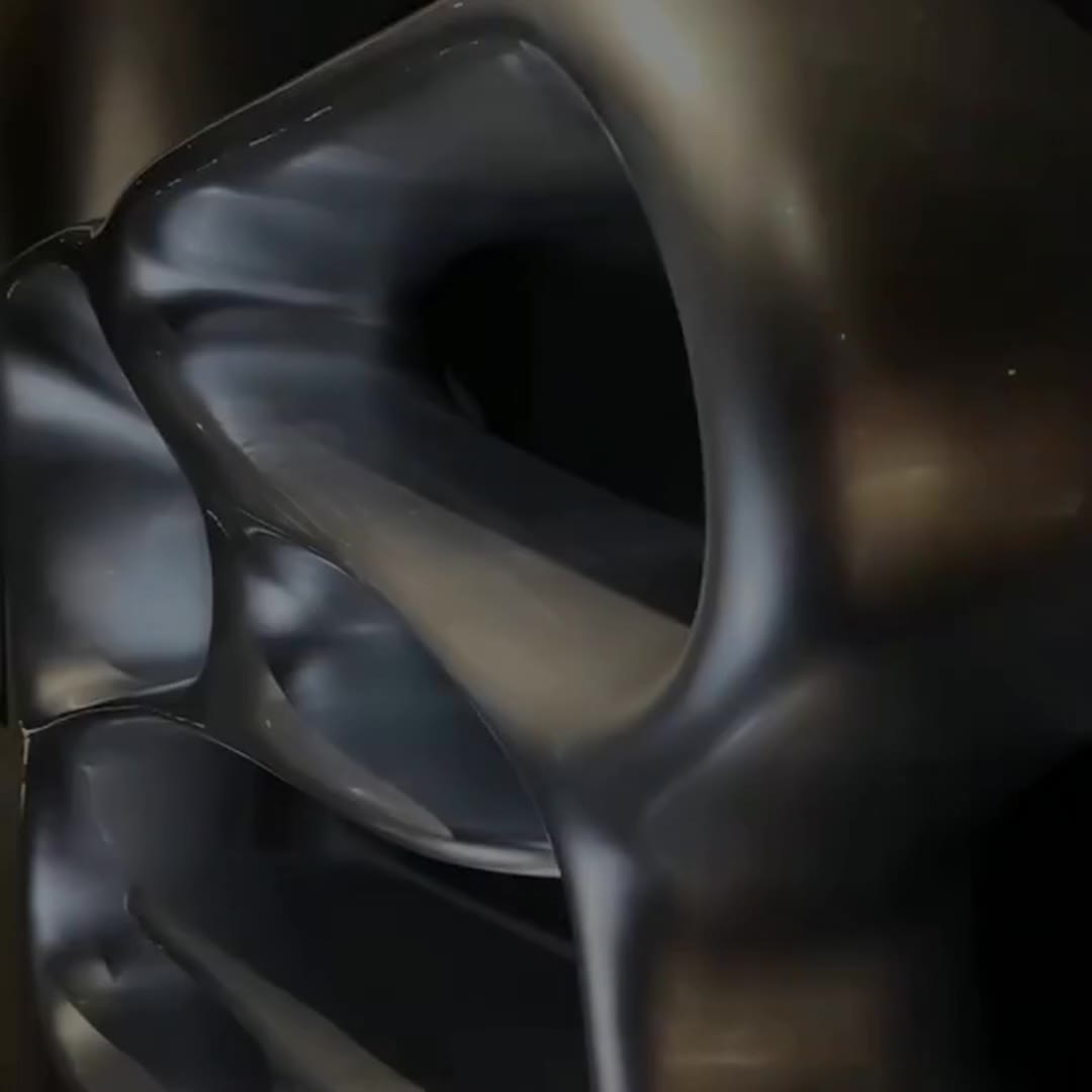 Close-up of a smooth oval void cut through a mirror-polished stainless steel organic shelf, reflecting the dark surroundings