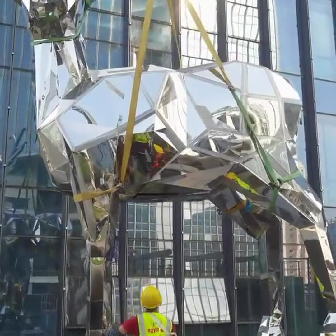 Mirror stainless steel deer body on lifting straps with the city reflected in the facade panels