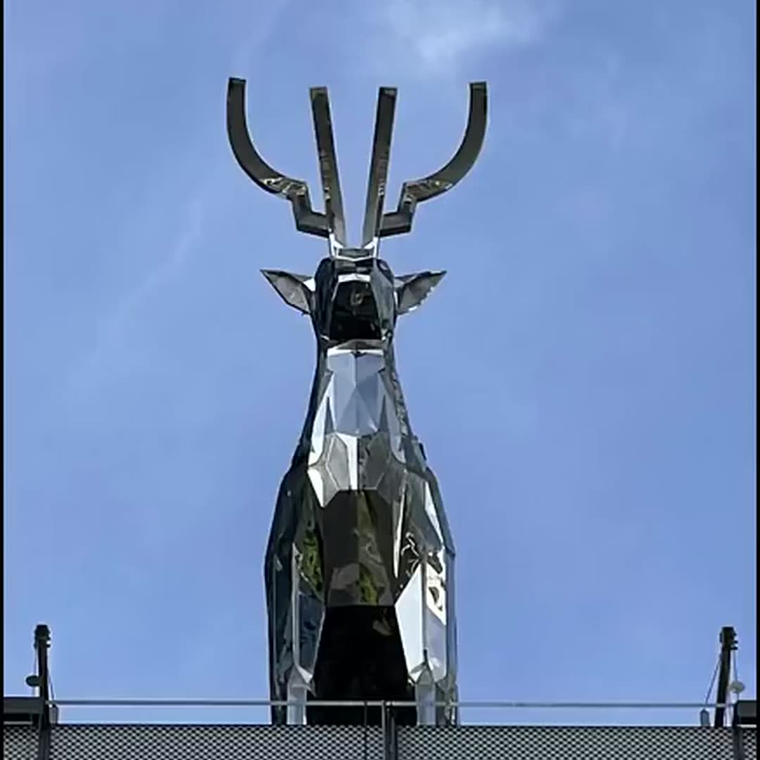 Completed faceted mirror stainless steel deer standing on a rooftop parapet against the sky