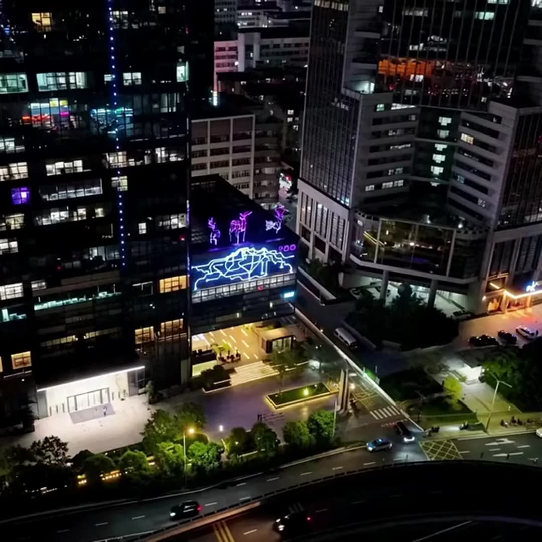 Night aerial view of the city block with the deer outline lighting glowing purple above the streets