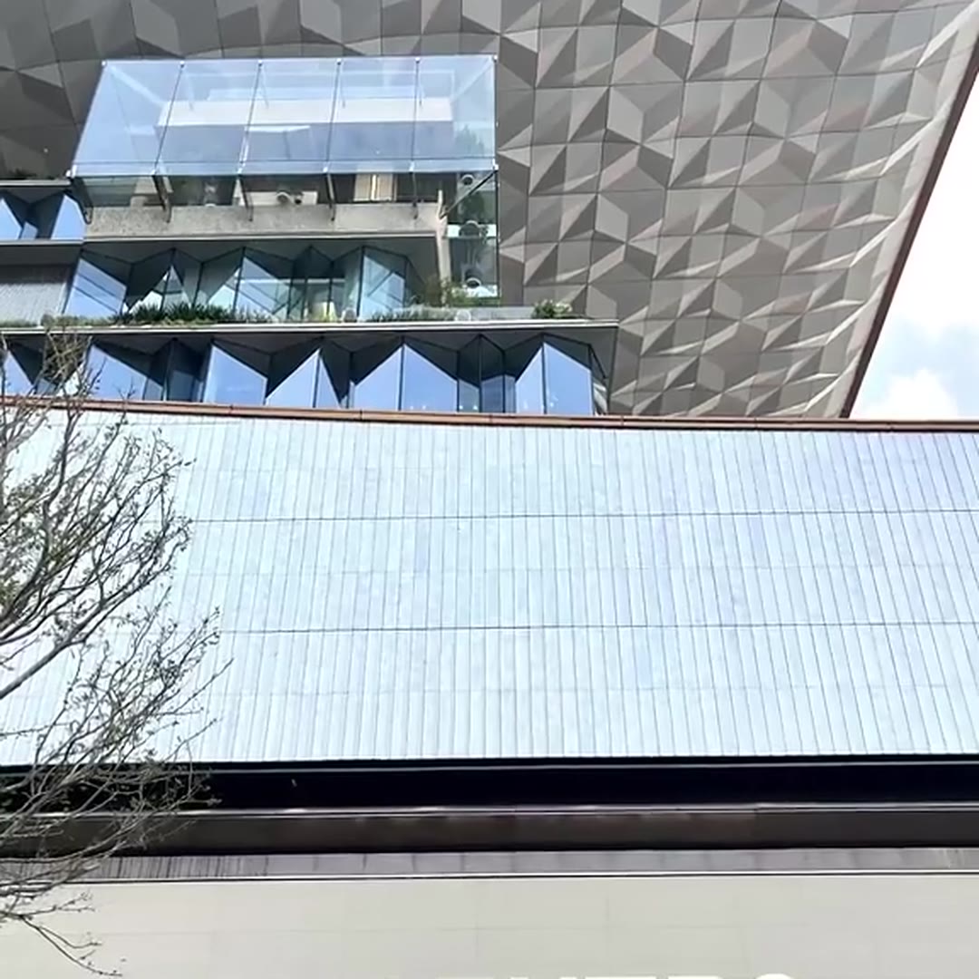 Bright daytime detail of the faceted stainless steel surface wrapping a glazed terrace volume on a commercial building