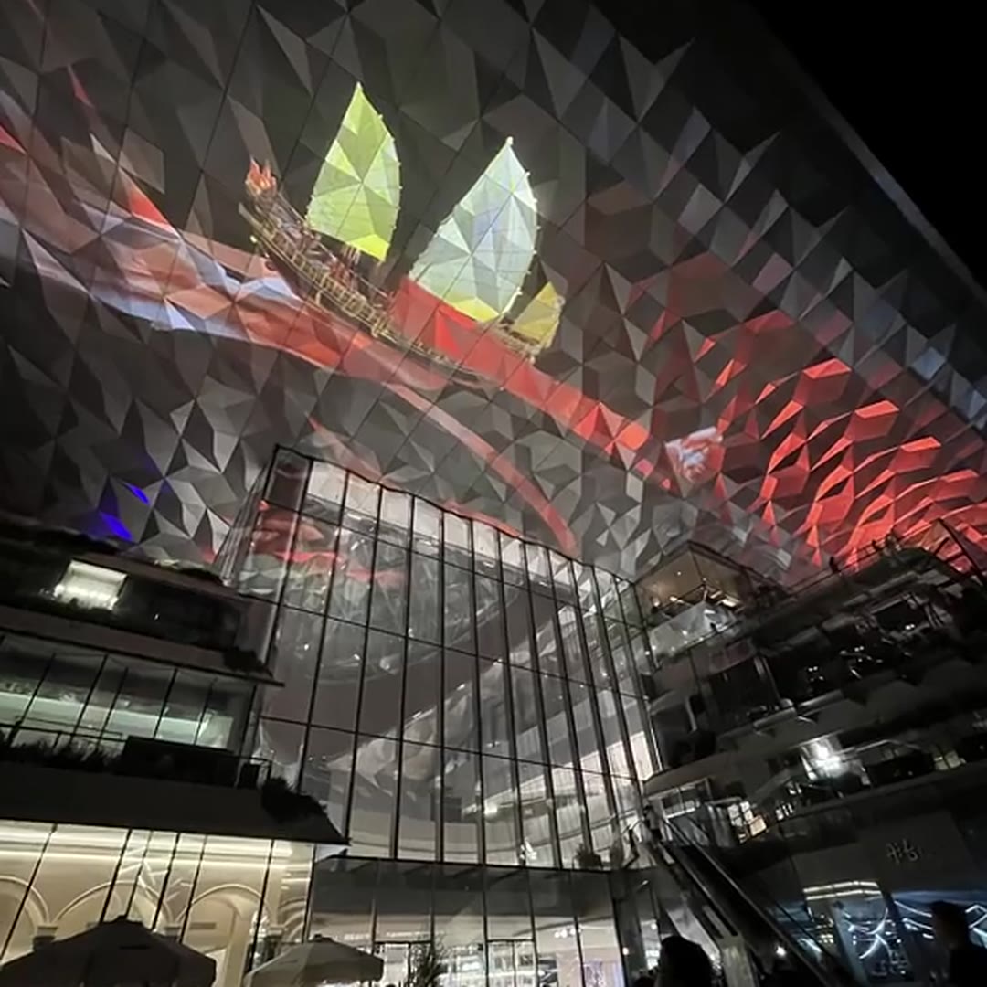 Faceted stainless steel ceiling taking a dynamic red and yellow RGB media-mapping projection above a glass atrium wall