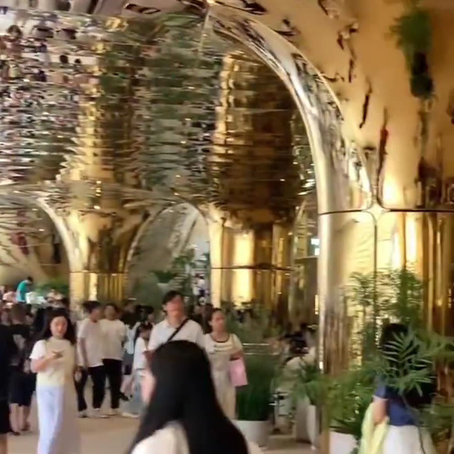 Mall walkway lined with champagne-gold mirror stainless steel columns and arched mirrored ceilings reflecting warm storefront lighting