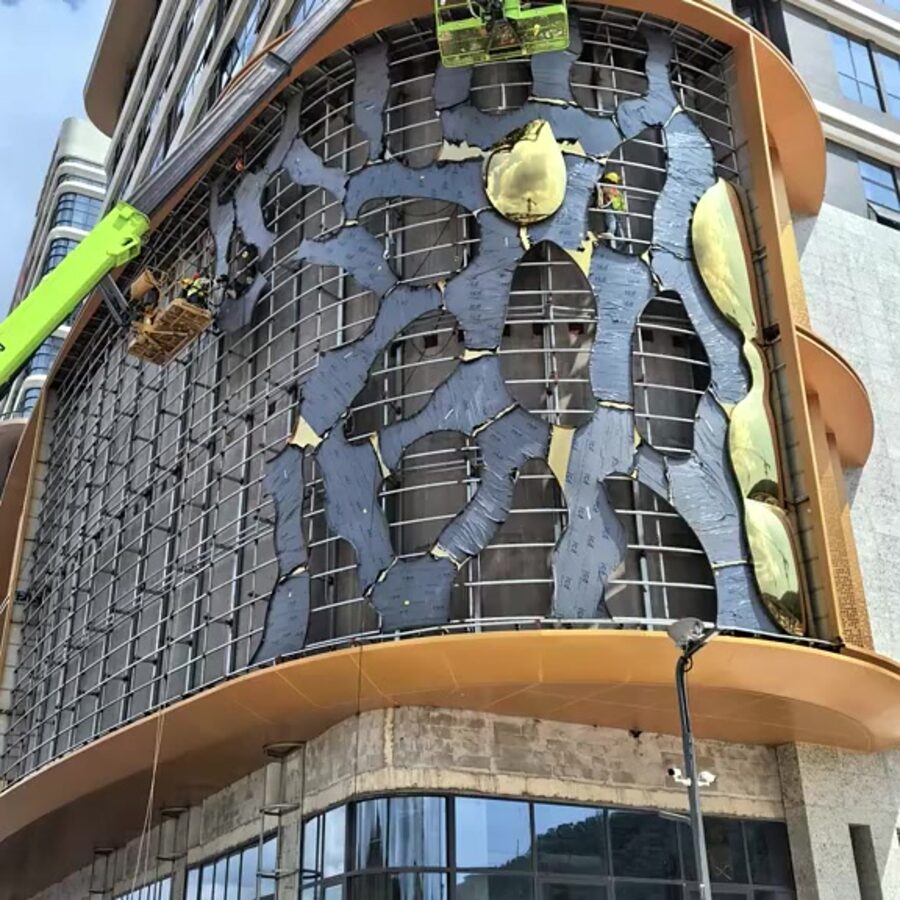 Gold-toned stainless steel panels installed on a curved high-rise corner under construction