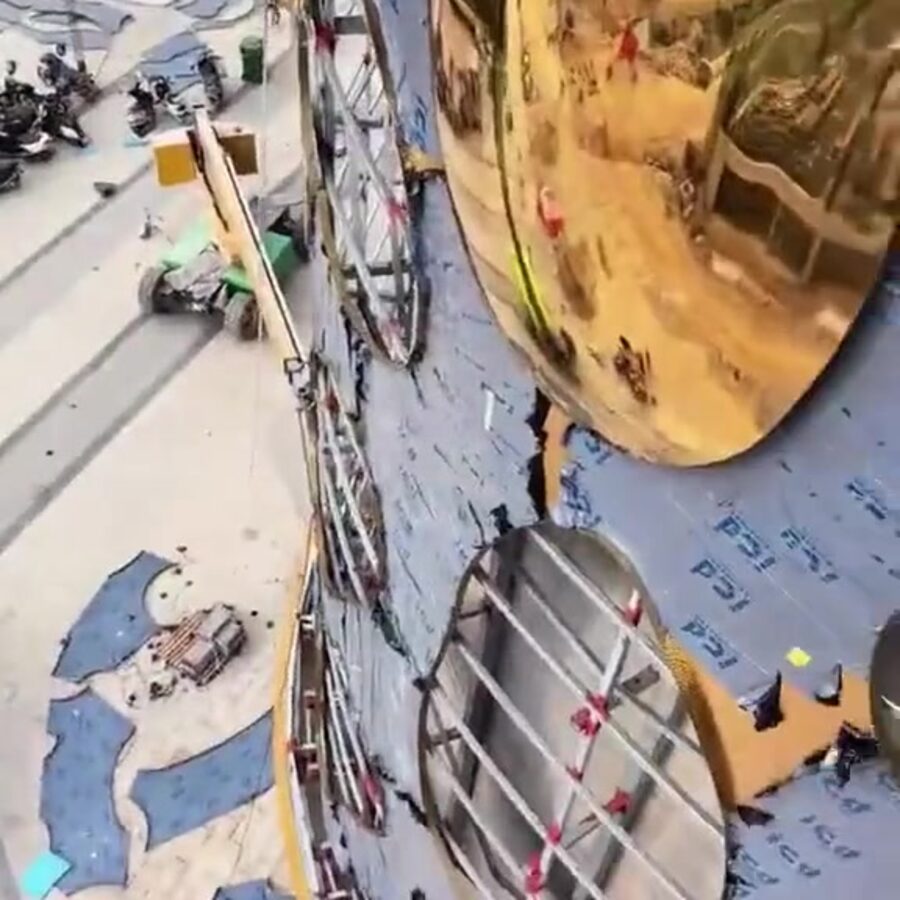 Aerial view of a large mirror stainless steel panel being installed on the tower facade