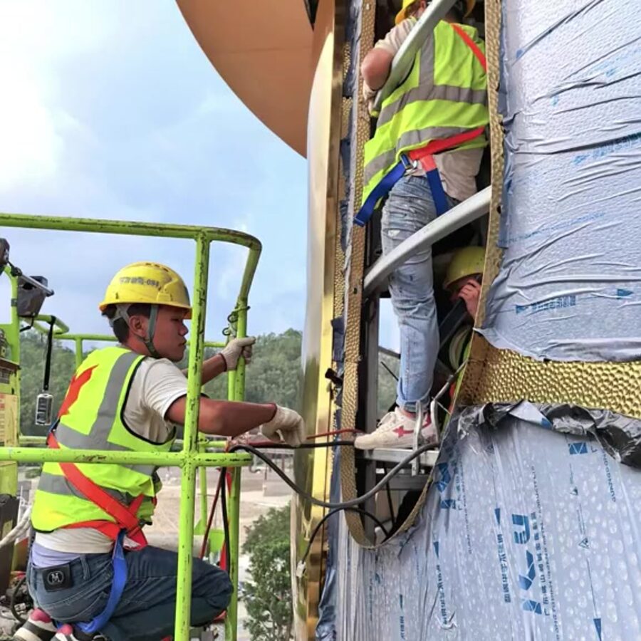 Installers in safety harnesses mounting mirror stainless steel facade panels on a high-rise tower