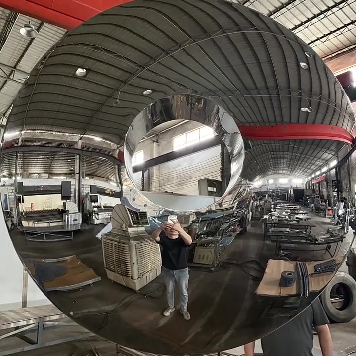 Full view of a mirror-polished stainless steel ring sculpture with a worker standing beside it to show scale