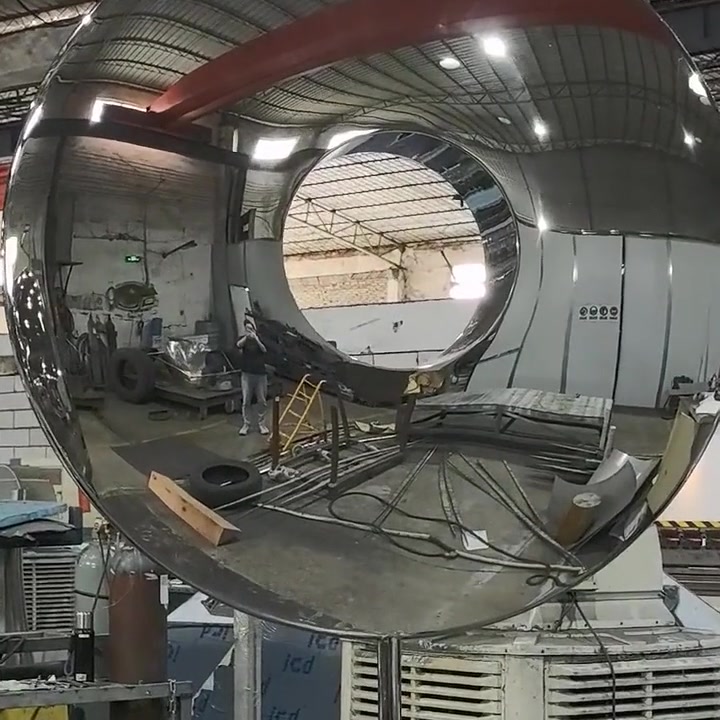 The ring sculpture reflecting the workshop roof trusses, red overhead crane beams and machinery across its mirror surface