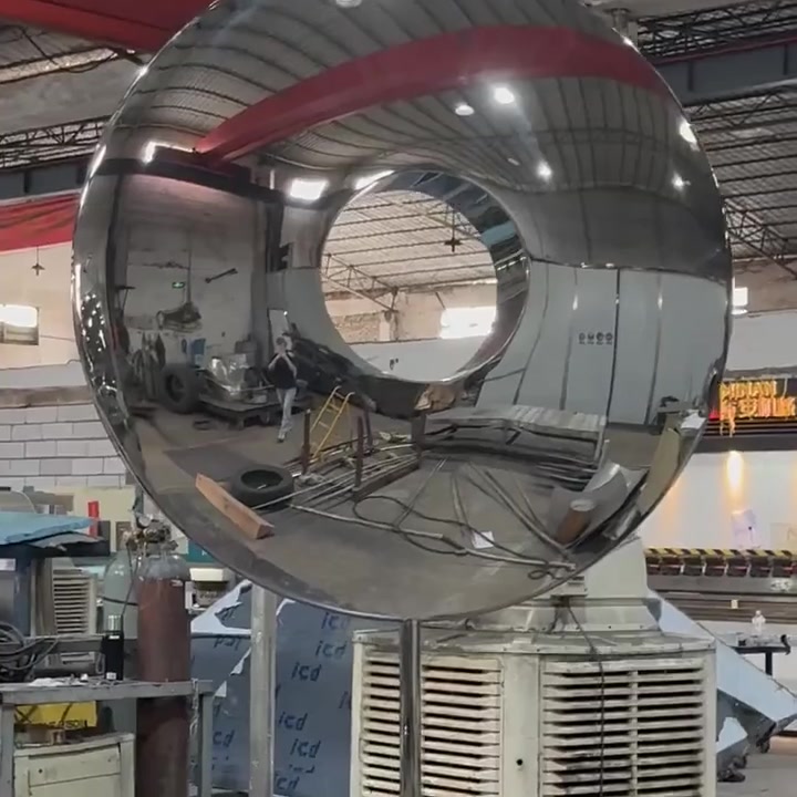 Mirror-polished stainless steel ring sculpture photographed from a low angle, reflecting the workshop ceiling and lighting