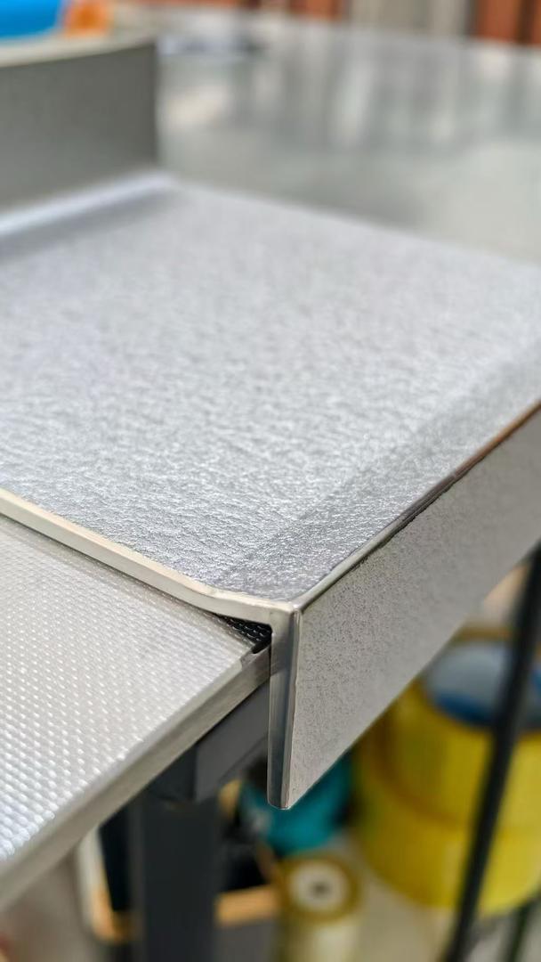 Detail of a folded corner on a scratch-resistant stainless steel countertop showing the textured top surface, square folded edge and ground finish
