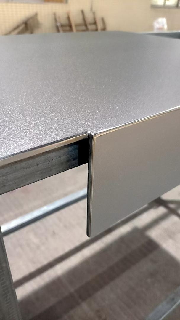 Fabricated scratch-resistant stainless steel worktable with a square folded edge and matte textured top, standing on a steel frame in a workshop
