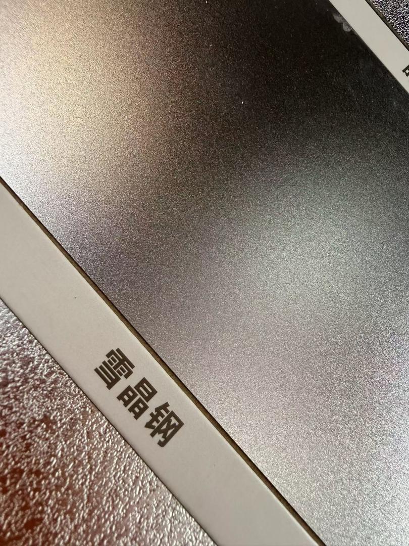 Close-up of a fine matte etched stainless steel sheet sample in dark gunmetal grey, showing a dense even anti-scratch grain