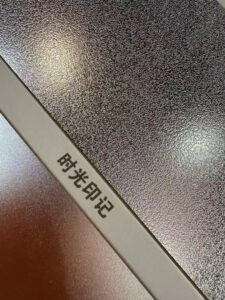 Close-up of an embossed stainless steel sample sheet labelled anti-scratch, showing a coarse hammered relief surface next to a fine matte finish