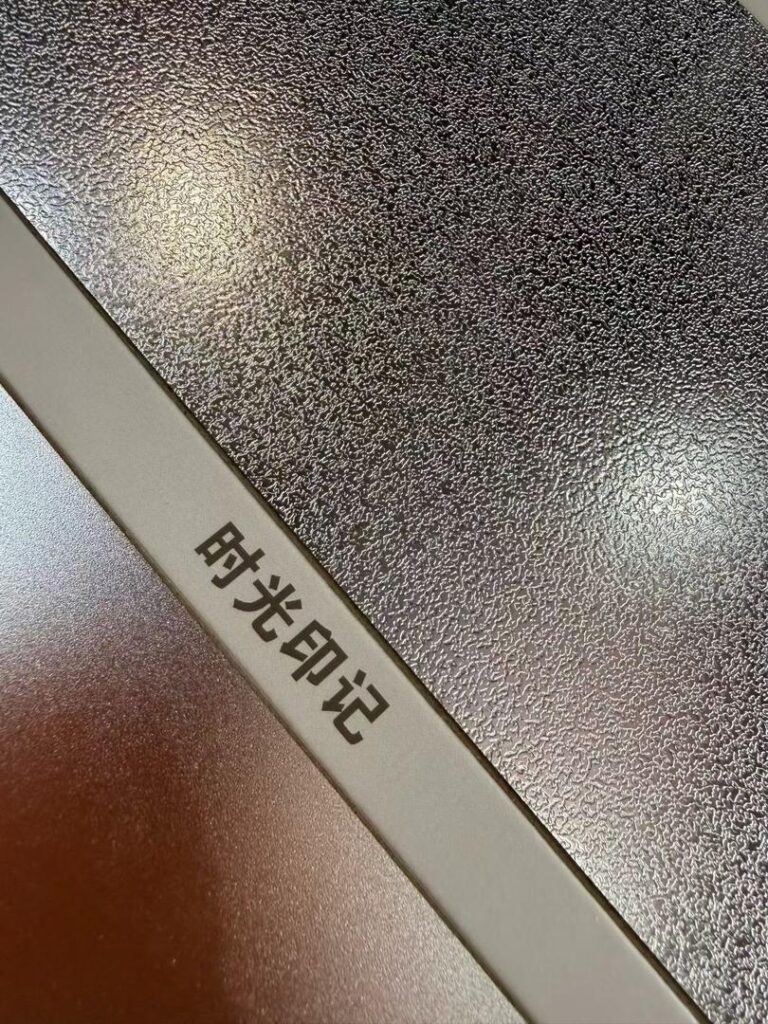 Close-up of an embossed stainless steel sample sheet labelled anti-scratch, showing a coarse hammered relief surface next to a fine matte finish