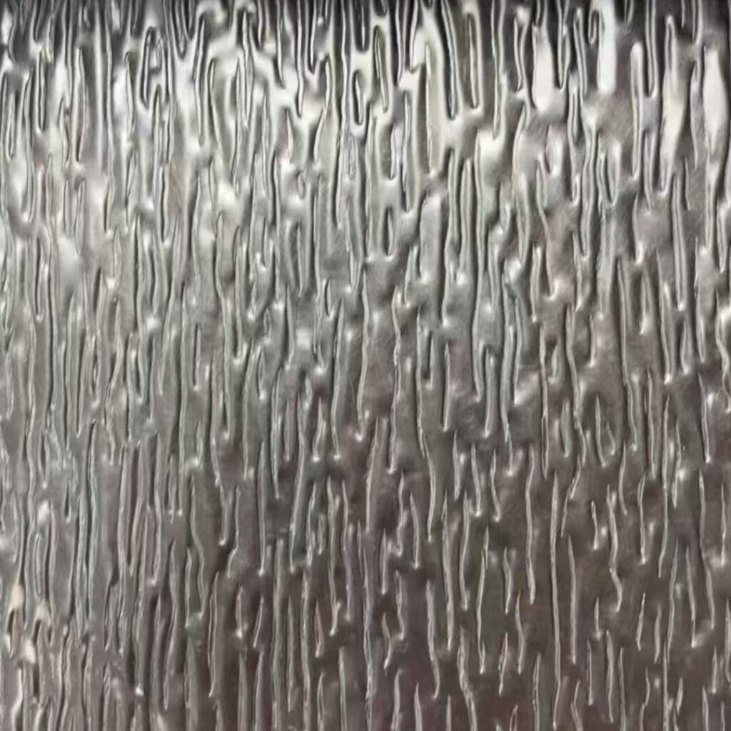 Close-up of a stainless steel sheet embossed with a tree bark relief, showing dense irregular vertical grooves that break the surface into ridges and hollows