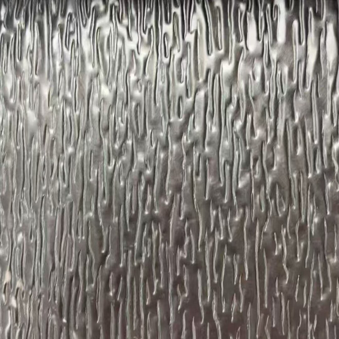 Close-up of a stainless steel sheet embossed with a tree bark relief, showing dense irregular vertical grooves that break the surface into ridges and hollows