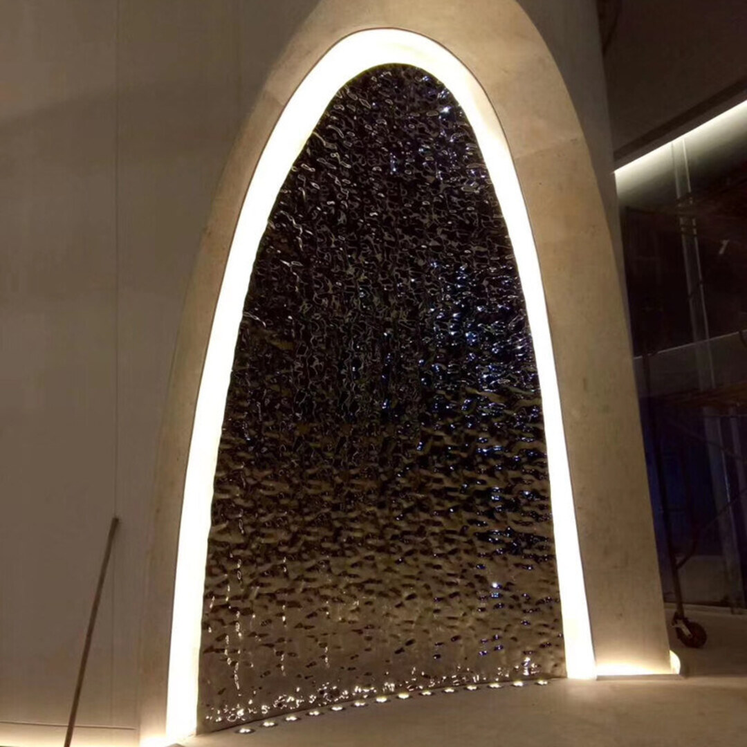 A pointed arch feature panel filled with a heavily textured stainless steel sheet, halo-lit around the arch reveal so the relief reads in shadow and highlight