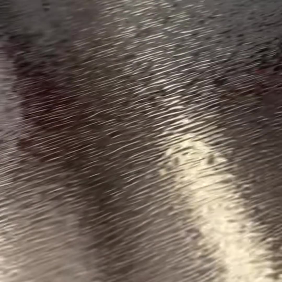Macro frame from the film: the same embossed stainless steel surface as the light moves, the highlight sliding down the valleys and flattening the texture momentarily